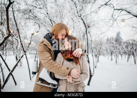 Winter und Datum. Junges Paar in der Liebe mit Mann und Frau im Winter gegen den Hintergrund der schneebedeckten Bäume im Park umfassen. Ein Kerl mit langen h Stockfoto
