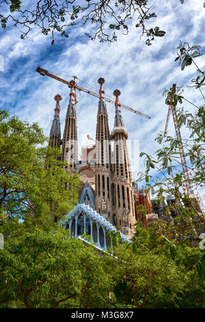 BARCELONA, SPANIEN - 13. MAI 2017: Die Sagrada Familia von Bäumen und einem schönen blauen Himmel umgeben, gesehen von der Gaudi. Stockfoto