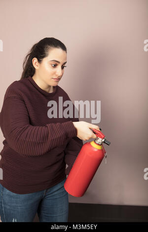 Bestimmt Frau mit einem roten Feuerlöscher wies vor ihr auf den Boden im Innenraum in einem Gebäude Stockfoto