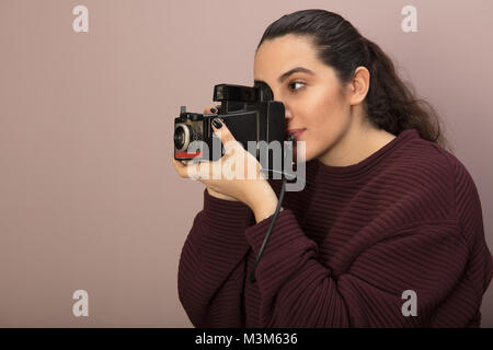 Junge Frau Fotograf ein Foto mit einem Vintage Kamera konzentriert sie sich auf Ihr Thema in Seitenansicht Stockfoto