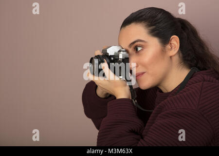 Junge Frau Fotograf ein Foto mit einem Vintage Kamera konzentriert sie sich auf Ihr Thema in Seitenansicht Stockfoto
