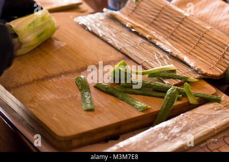 Der Koch schneidet eine Gurke mit einem Messer auf Holzbrett Stockfoto