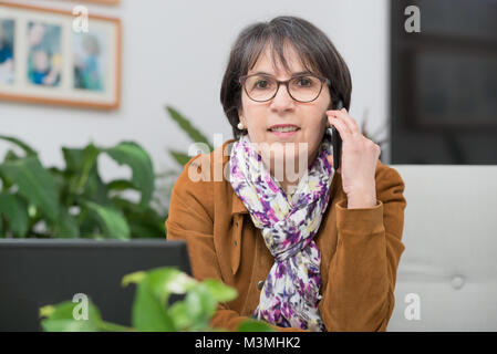 Charmante reife Frau mit braunen Jacke am Telefon sprechen zu Hause Stockfoto