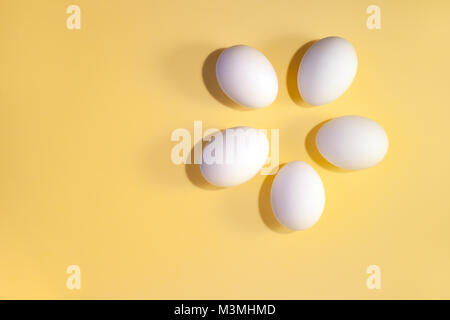 Flach Minimalismus. Fünf weiße Eier liegen im Kreis auf einem gelben Hintergrund mit kopieren. Stockfoto