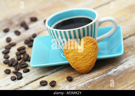 Crunchy Cookie in Form von Herzen lehnte sich gegen die Tasse Kaffee auf Holzmöbeln im Landhausstil Oberfläche Stockfoto