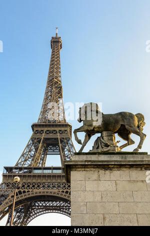 Low Angle Blick auf den Eiffelturm in Paris, von der Iena Brücke gegen den blauen Himmel gesehen, mit einem Equestrian Stein Statue im Vordergrund. Stockfoto