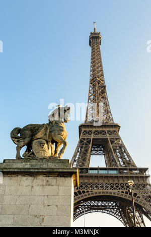 Low Angle Blick auf den Eiffelturm in Paris, von der Iena Brücke gegen den blauen Himmel gesehen, mit einem Equestrian Stein Statue im Vordergrund. Stockfoto