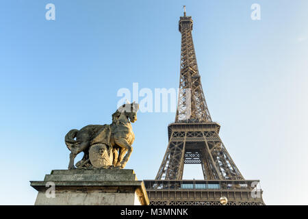 Low Angle Blick auf den Eiffelturm in Paris, von der Iena Brücke gegen den blauen Himmel gesehen, mit einem Equestrian Stein Statue im Vordergrund. Stockfoto