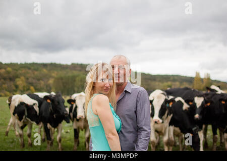 Im freien Portrait der Bauer und seine Frau umarmt vor Ihre Schwarz-weiße Kühe. Stockfoto