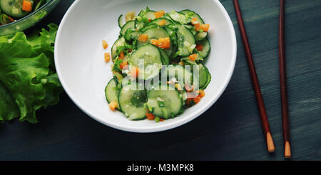 Chinesischer Gurkensalat auf dem weißen Teller. Ansicht von oben. Stäbchen. Asiatische Küche. Paprika, Gurke und Sesam. Breite Foto. Vegetarisches Gericht. W Stockfoto