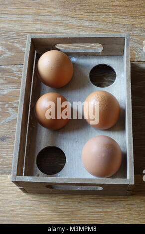 Vier braune Eier in eine Holzkiste mit Platz für sechs Eier, in natürlichem Licht. Stockfoto