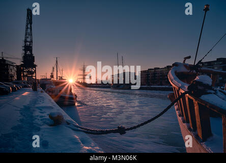 Landschaftlich schöne Blick auf die Boote auf der Aura Fluss in Telakkaranta im Winter Sonnenuntergang mit Schwan von Finnland im Hintergrund in Turku, Finnland verankert Stockfoto