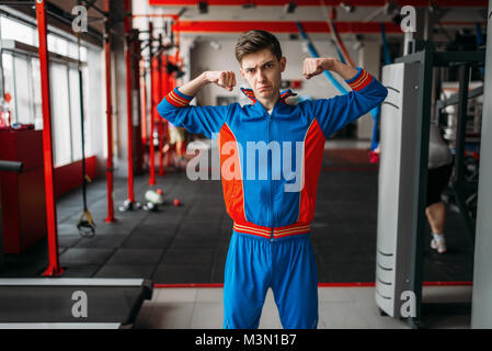 Dünne Mann in Sportswear zeigt seine Muskeln an der Turnhalle, Humor. Männliche Person im Sport Club schwach Stockfoto