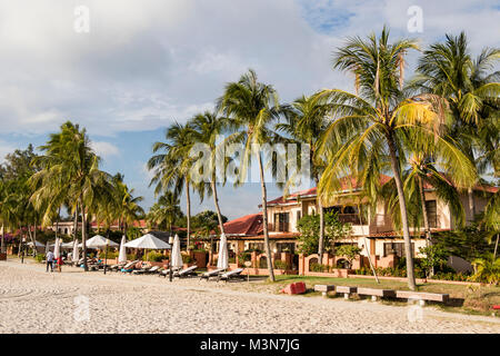 Langkawi, Malaysia, 21. Dezember 2017: weiße Sandstrand von Langkawi mit Palmen und Bungalows im Hintergrund vor dem Sonnenuntergang Stockfoto