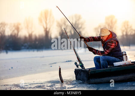 Happy alter Fischer fangen Fische auf dem gefrorenen Fluss im Winter Stockfoto