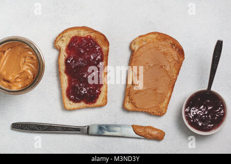 Zwei Toast mit Erdnussbutter und Marmelade auf einem hellgrauen konkreten Hintergrund. Ansicht von oben Stockfoto