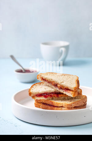 Toast mit Erdnussbutter und Marmelade in einem weißen Keramikplatte auf einem blauen konkreten Hintergrund Stockfoto
