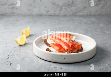Sandwich mit Lachs, Frischkäse und Roggen Brot in eine weiße Platte auf einem grauen konkreten Hintergrund Stockfoto