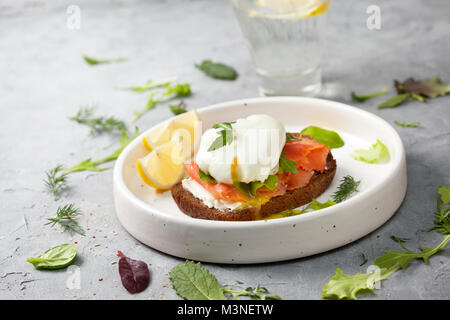 Sandwich mit Lachs, Frischkäse, Eier und Gruene haben sich auf einen weissen Teller auf einem grauen konkreten Hintergrund Stockfoto