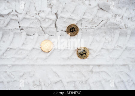 Copprito Münzen aus Gold bitcoin liegen auf dem Schnee. Niemand benötigt. Im Winter auf der Straße, Spuren von Autos. Stockfoto