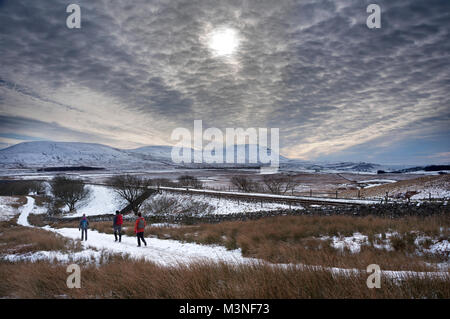 Trübe Winter Sonne über Wanderer neben der Settle-Carlisle Railway, Ribblehead. Ingleborough Peak ist am Horizont. Yorkshire Dales National Park, Großbritannien. Stockfoto