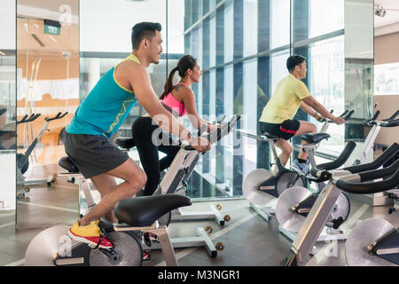 Stattlich und selbstbewussten jungen Mann lächelnd, während bei der Gruppe der Klasse von Hiit indoor cycling Radeln in einem modernen Fitness Club Stockfoto