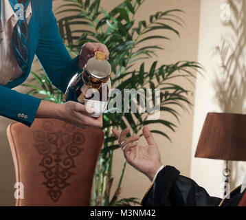 Kellnerin serviert arabischen Kaffee zu einem wohlhabenden saudi-arabischer Mann Stockfoto