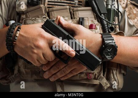 Close-up of a gun, die ordnungsgemäß einen Mann in einem militärischen Wüste einheitliche und Body Armour hält auf einem schwarzen Hintergrund im Studio. Stockfoto