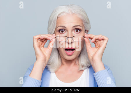 Close up Portrait von stilvollen, gealtert, charmant, überrascht, schockiert Frau mit Ösen peek Gläser mit weit geöffneten Augen und Mund über Graues backgr heraus Stockfoto