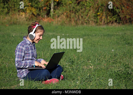 Glückliche kleine Mädchen spielen Laptop und das Hören von Musik über Kopfhörer Stockfoto