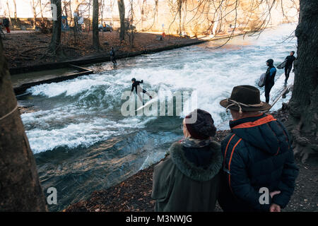 München, Deutschland - Dezember 7, 2017: Ältere Paare zusehen, wie Surf ride künstliche Welle am Eisbach, gefährliche Wasser Isar Kanal bei Englischen Stockfoto