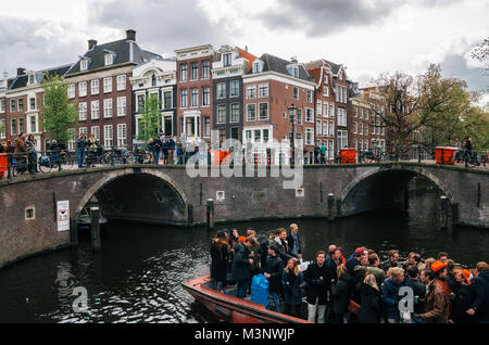 Amsterdam, Niederlande - 25 April 2017: Einheimische und Touristen Fahrt auf Boote unter schmalen Brücken und bei der Feier King's Tag zusammen teilnehmen Stockfoto