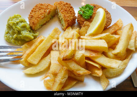 Ein Café das Mittagessen von geräuchertem Schellfisch Fischfrikadellen mit Pommes frites Erbsenpüree, einer Scheibe Zitrone und Petersilie garnieren Fisch Kuchen aufgeschnitten Stockfoto