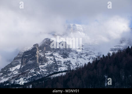 Majestic Alpine Szene mit Wald bedeckten Hang und schneebedeckten Berggipfeln Piercing der dichter Nebel und Wolken Stockfoto