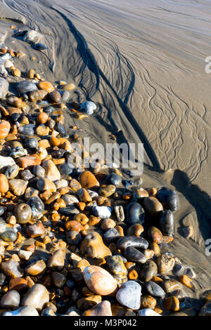 Kies und Kieselsteinen Neben nassem Sand in der Sonne Stockfoto