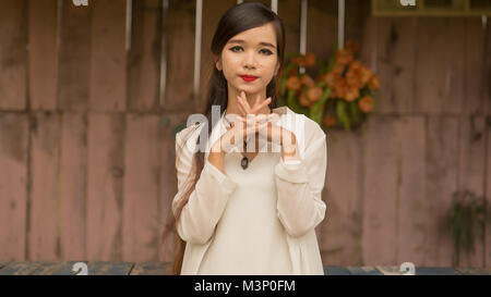 Vietnamesische junge brunette Mädchen mit langen Haaren posing gegen die Wand mit künstlichen Rosen. Hanoi. Stockfoto