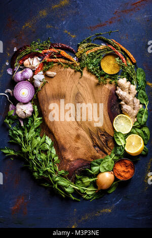 Blick von oben auf die Herzen von Kräutern, Gemüse und Gewürzen und Holz Schneidebrett auf Blau Stockfoto