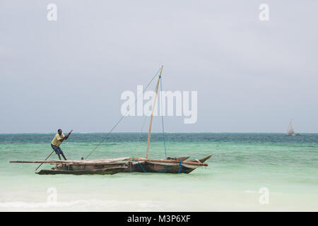 KIWENGWA, SANSIBAR - Dec 29, 2017: lokale Mann seinen traditionellen hölzernen Dhow Boot in der Nähe von Kiwengwa drücken, Sansibar Stockfoto