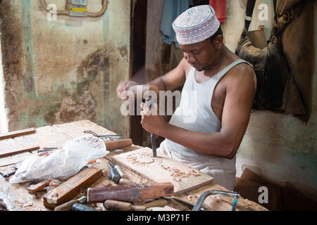 STONETOWN, SANSIBAR - Jan 1, 2018: Tischler erstellen Ornamente auf Holzbrett mit traditionellen Handwerkzeugen in Stonetown, Sansibar Stockfoto