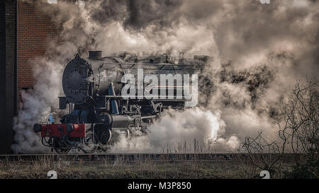 Eine Dampflok Lok taucht aus dem Nebel, Dampf und Rauch in einer Landschaft, die Seite zu sehen. Stockfoto