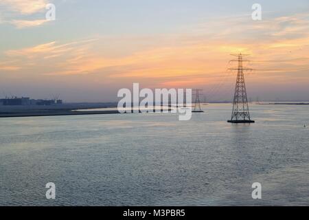 Hohe Spannung Strom Leistung Linien durch das Meer mit tollen bunten Wolken im Hintergrund verteilt. Stockfoto