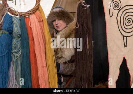 York, UK, 12. Februar 2018, Dame gekleidet wie ein Wikinger auf der jährlichen Jorvik Viking Festival. Um einen Marktstand, sie ist teilweise durch lange Stränge der bunten Wolle hängen auf dem Display ausgeblendet. Sie ist die Teilnahme an einem realistischen Re-enactment von Leben bei einem Viking Markt. Stadtzentrum von York, North Yorkshire, England, UK. Credit: Ian Lamond/Alamy leben Nachrichten Stockfoto