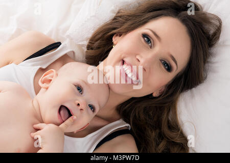 Glückliche Mutter und ihrem Baby Sohn auf einem Bett zusammen liegen. Glückliche Familie. Mutter und das Neugeborene portrait. Stockfoto