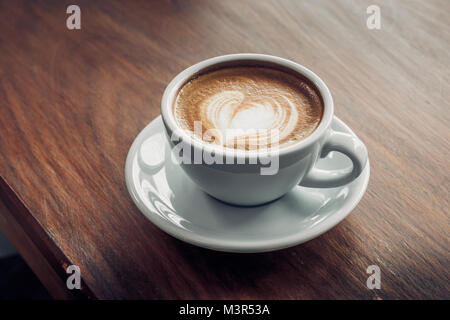 Close up heißen Cappuccino Tasse mit Herzform latte Kunst auf Holz Tisch im Cafe, Drak Tone Filter, Fuß- und Trinken Stockfoto