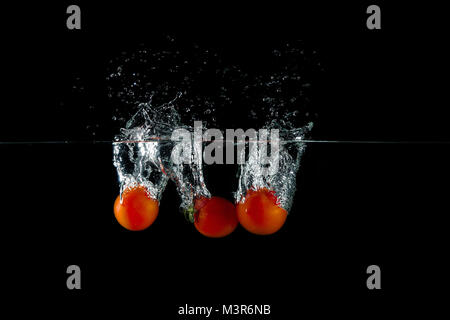 Gruppe von frischen roten Tomaten in Wasser spritzen auf schwarzem Hintergrund Stockfoto