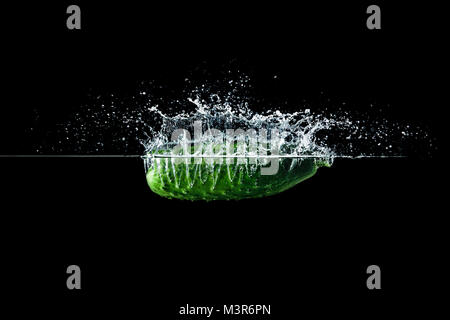 Frische, grüne Gurke im Wasser mit Spritzen auf schwarzem Hintergrund Stockfoto