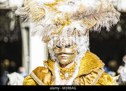 Porträt einer schönen Frau in einem gelben Kleid und goldene Maske mit Federn und Perlen während des Venezianischen Karnevals party in San Marco Platz Stockfoto