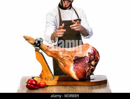 Chef lächelt Pointing Finger an der Kamera, in der Nähe des Tisches, an dem Ständigen steht eine große leckere geräucherte Bein von einem Schwein Stockfoto