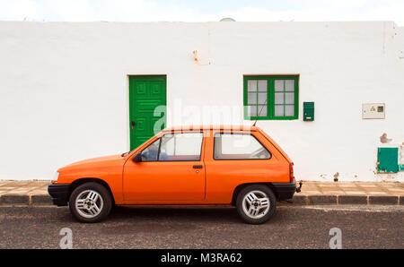 Arietta, Lanzarote/Spanien: Farben von Lanzarote, ein helles Orange altes Auto vor dem typischen weißen Haus mit der grünen Tür und Fenster geparkt Stockfoto