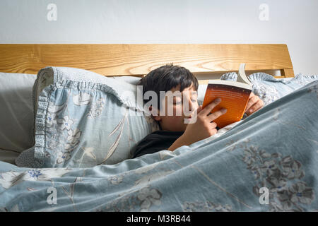 Junge mit einem Buch im Bett,, Großbritannien Stockfoto